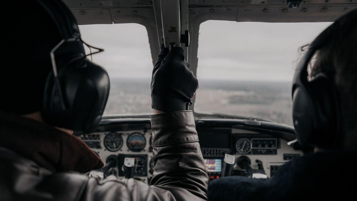 Two pilots operating a small aircraft from the cockpit with clear dashboard view.