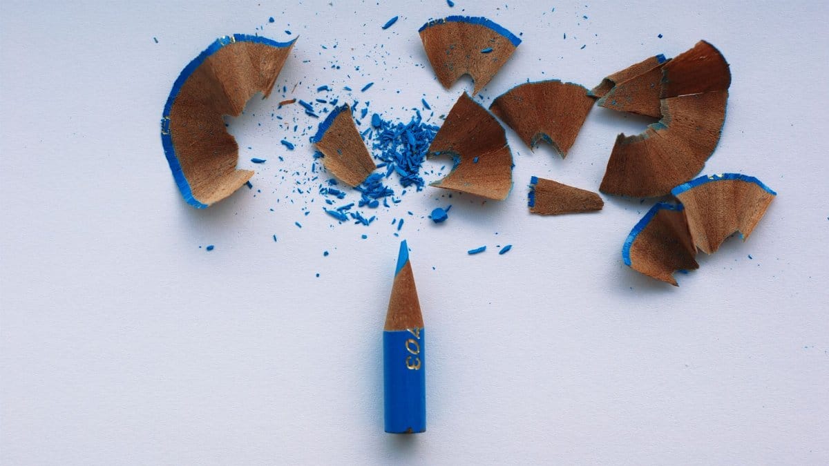 A sharpened blue pencil with wood shavings and colored dust on a white surface.