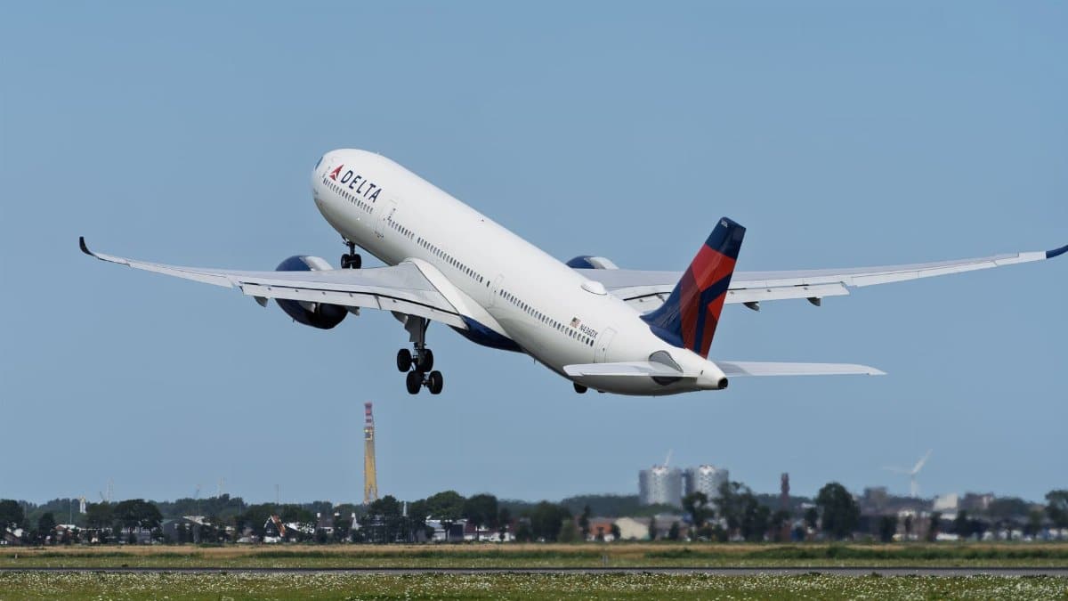 Delta Air Lines airplane taking off against a clear blue sky with cityscape background.
