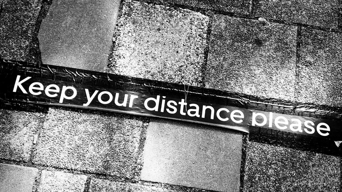 From above of warning sign attached to stone tiled floor in street of city during pandemic time in center of town