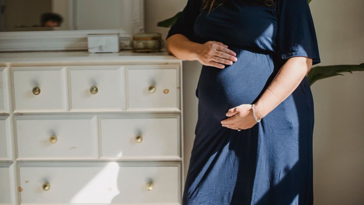Crop anonymous expectant female caressing gently belly near commode in house room in sunlight