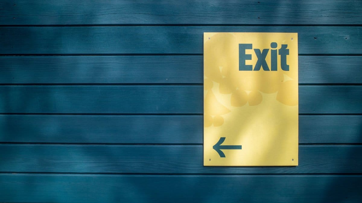 A yellow exit sign with an arrow on a blue wooden wall, suggesting direction.