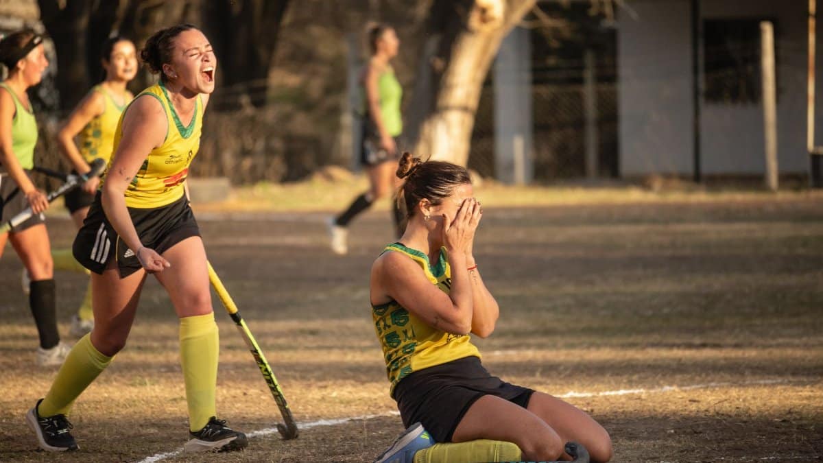 Field hockey players celebrating an emotional victory in a sunny outdoor match.