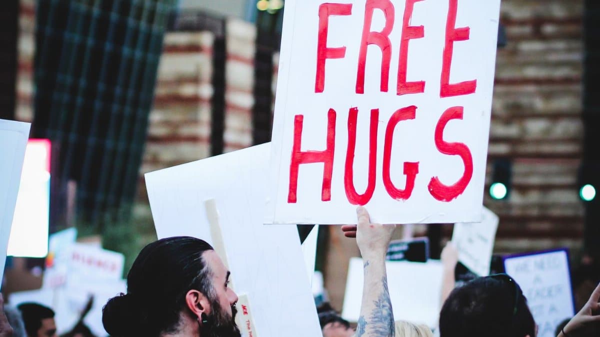 A lively street protest with a tattooed protester holding a 'Free Hugs' sign, exemplifying unity and peace.