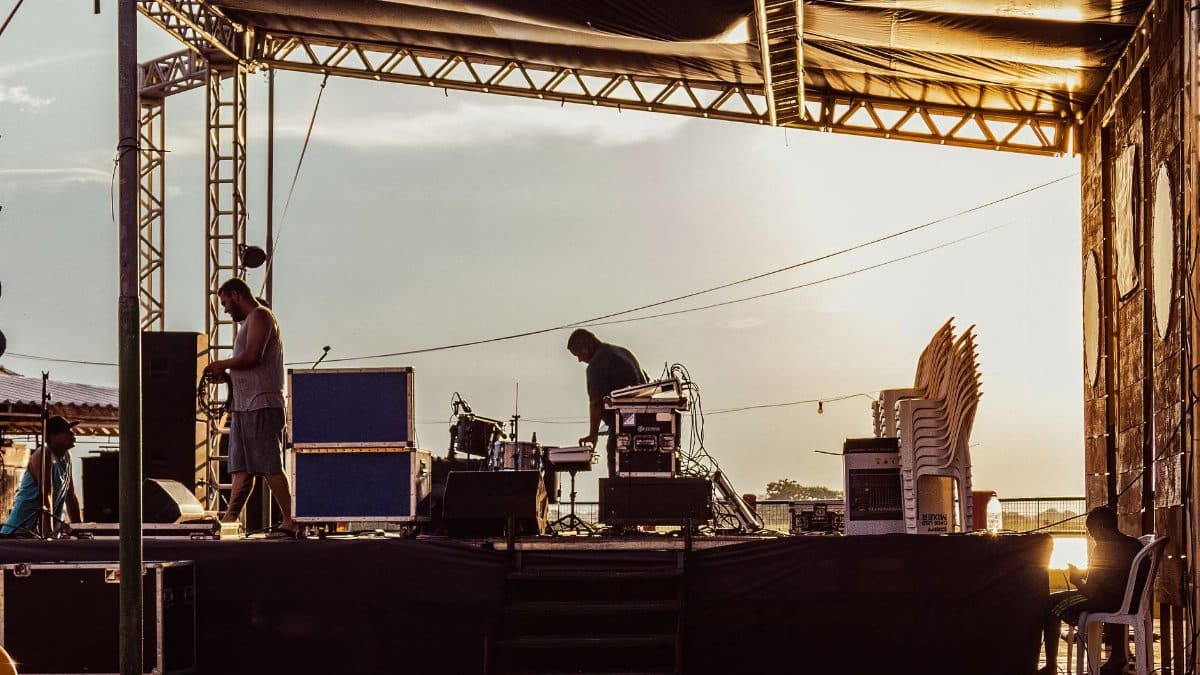 Musicians preparing outdoor stage during sunset with equipment and instruments.