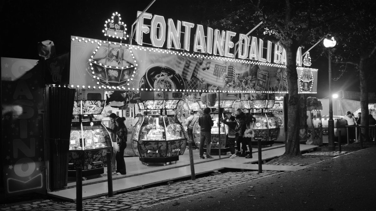 Monochrome night scene at a vibrant fair with arcade machines and lights.