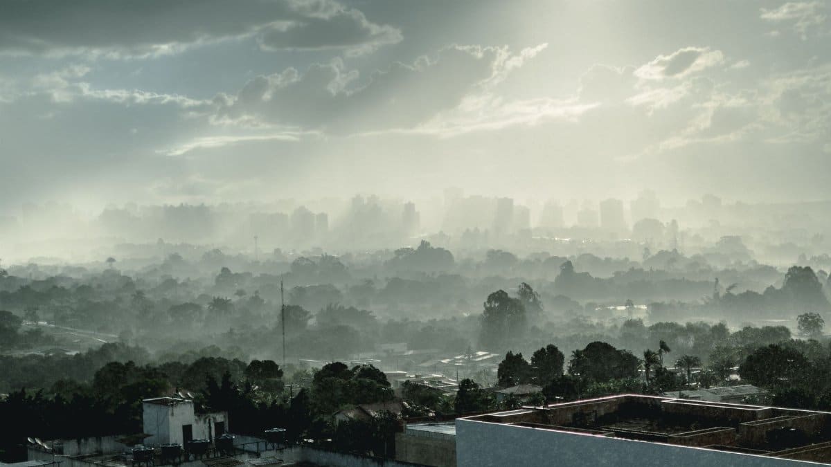 Misty cityscape of Brasília with fog enveloping buildings and trees under a cloudy sky.