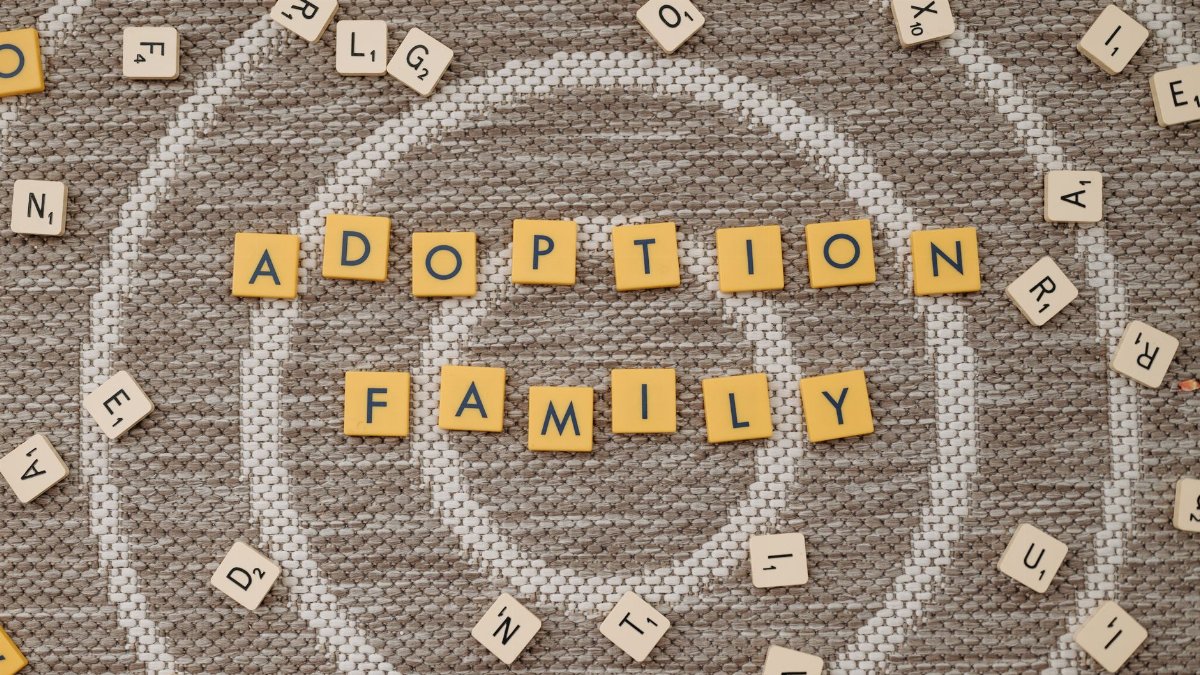 Top view of letter tiles spelling 'Adoption Family' on a textured floor.