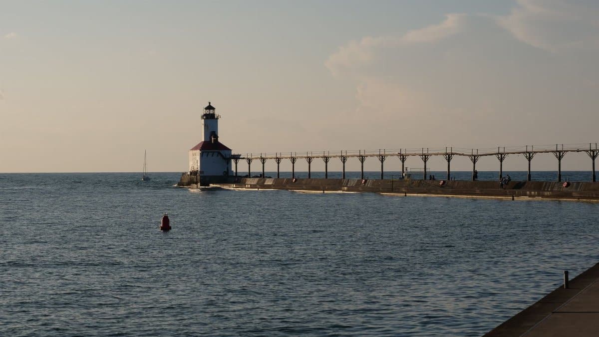 Peaceful view of Michigan City Lighthouse and pier at sunset over a calm lake.
