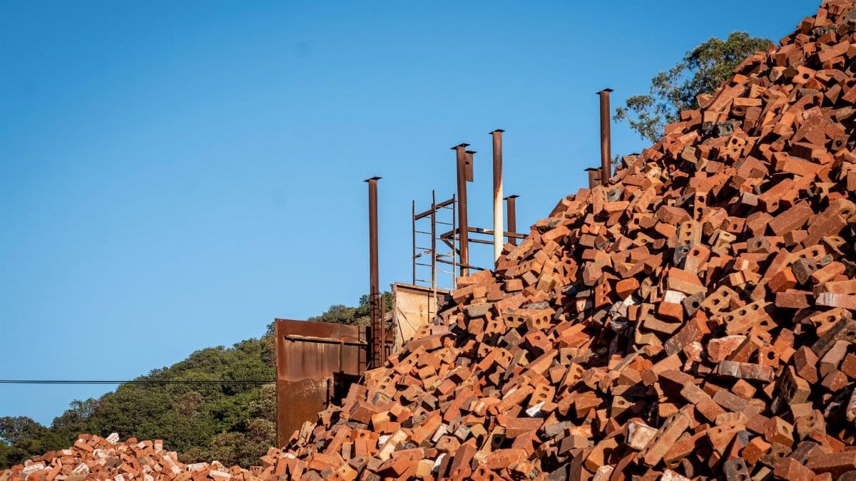 A towering pile of terracotta bricks under a clear sky at an outdoor construction site.