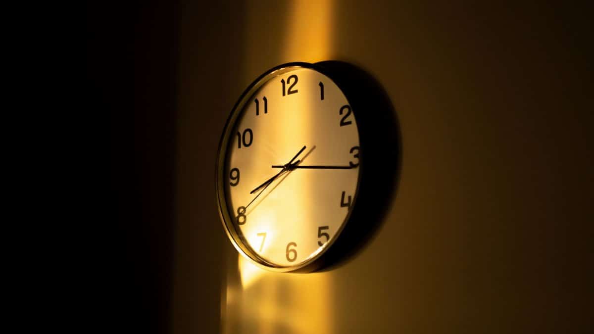 A wall clock illuminated by warm sunlight casts dramatic shadows, creating a contemplative mood.