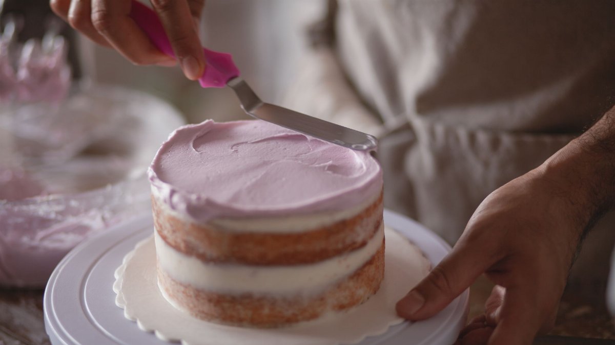 Close-up of a baker skillfully frosting a naked cake with pastel icing.