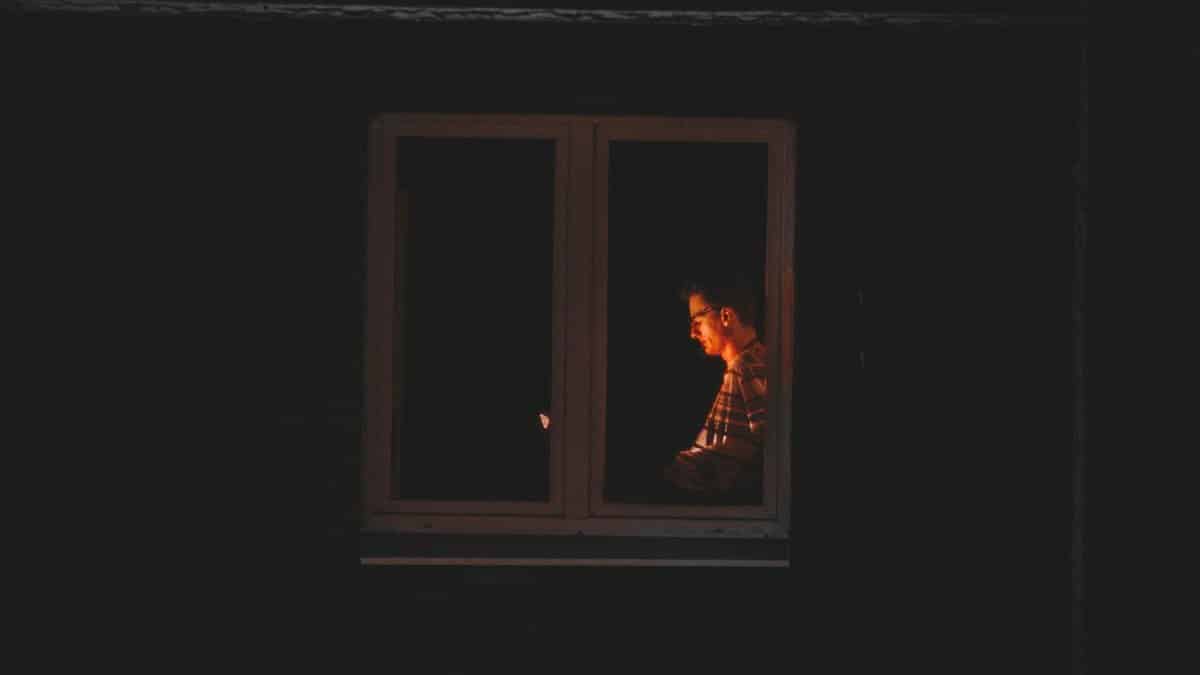 Silhouetted man working late at night in quiet solitude by window light.