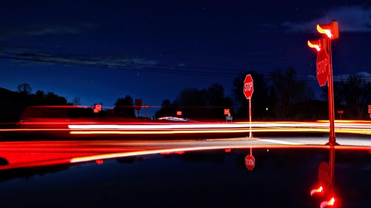 Red light trails from cars passing through a night intersection with stop signs.