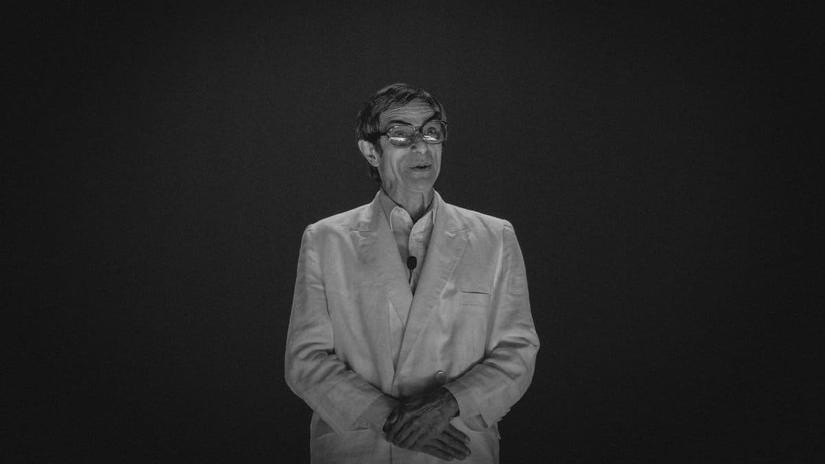 Elegant portrait of a man in a suit speaking at an event, captured in black and white.