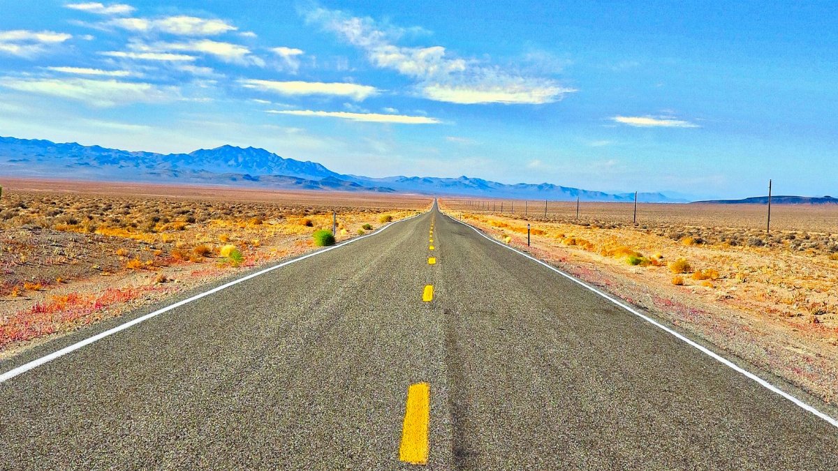 A long straight road in the Nevada desert under a blue sky, perfect for travel and adventure.
