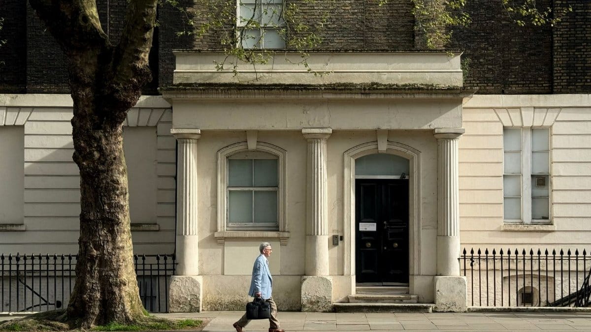 A man walks past a historic building facade in a city street, showcasing classic architectural elements.
