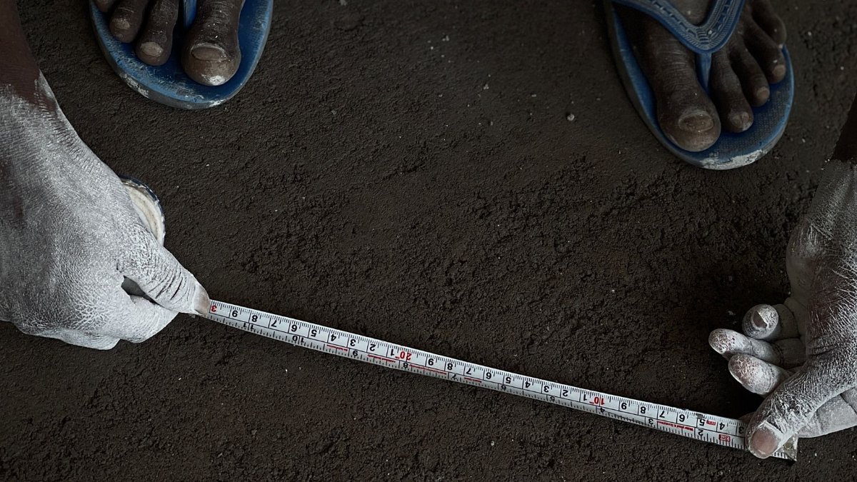 Close-up of a person measuring soil with a tape measure and chalk-covered hands.