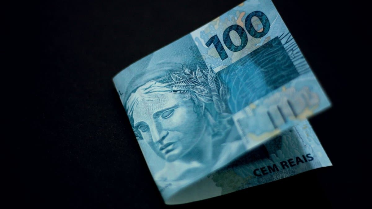 A Brazilian 100 real banknote displayed against a black backdrop, highlighting its design and color.