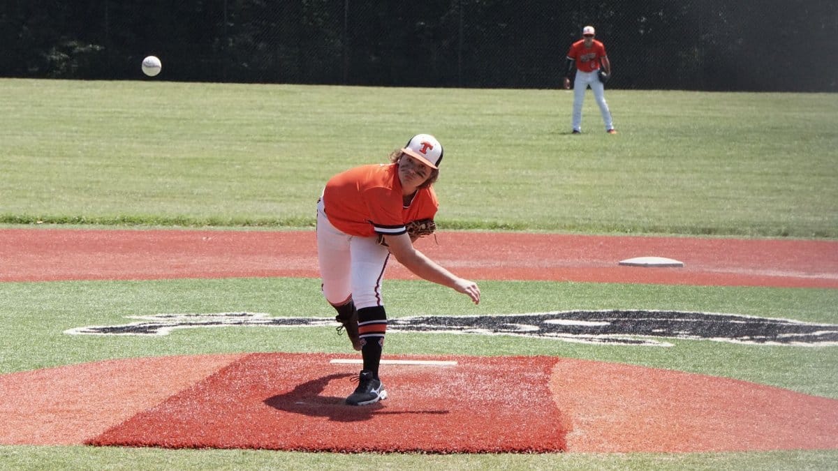 Young baseball pitcher throwing a pitch during a game on an outdoor field.