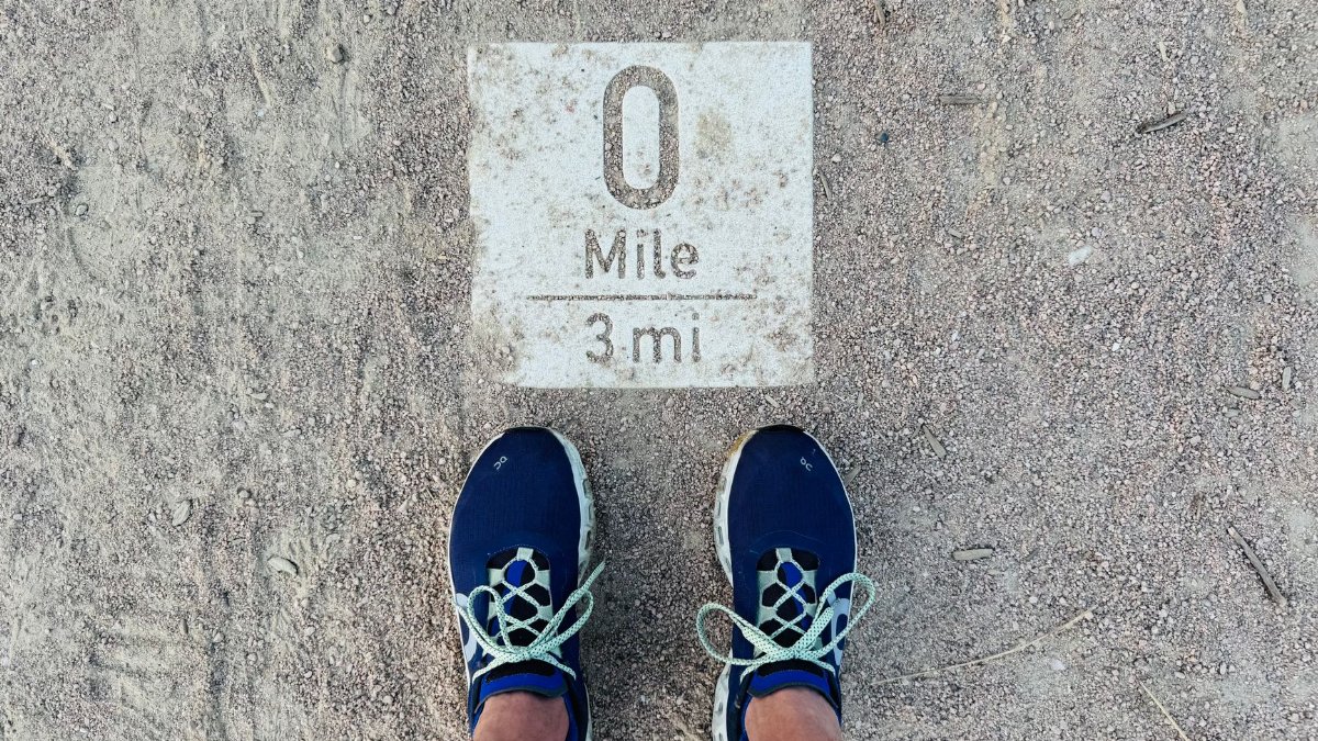 Close-up shot of blue running shoes at a 0 mile marker on a dusty path, symbolizing a journey's start.
