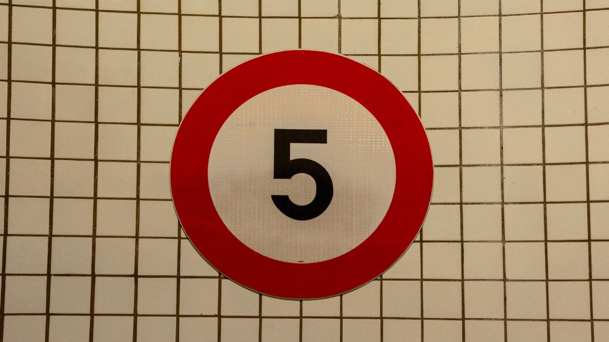 Close-up of a speed limit sign with the number 5 against a tiled wall background.