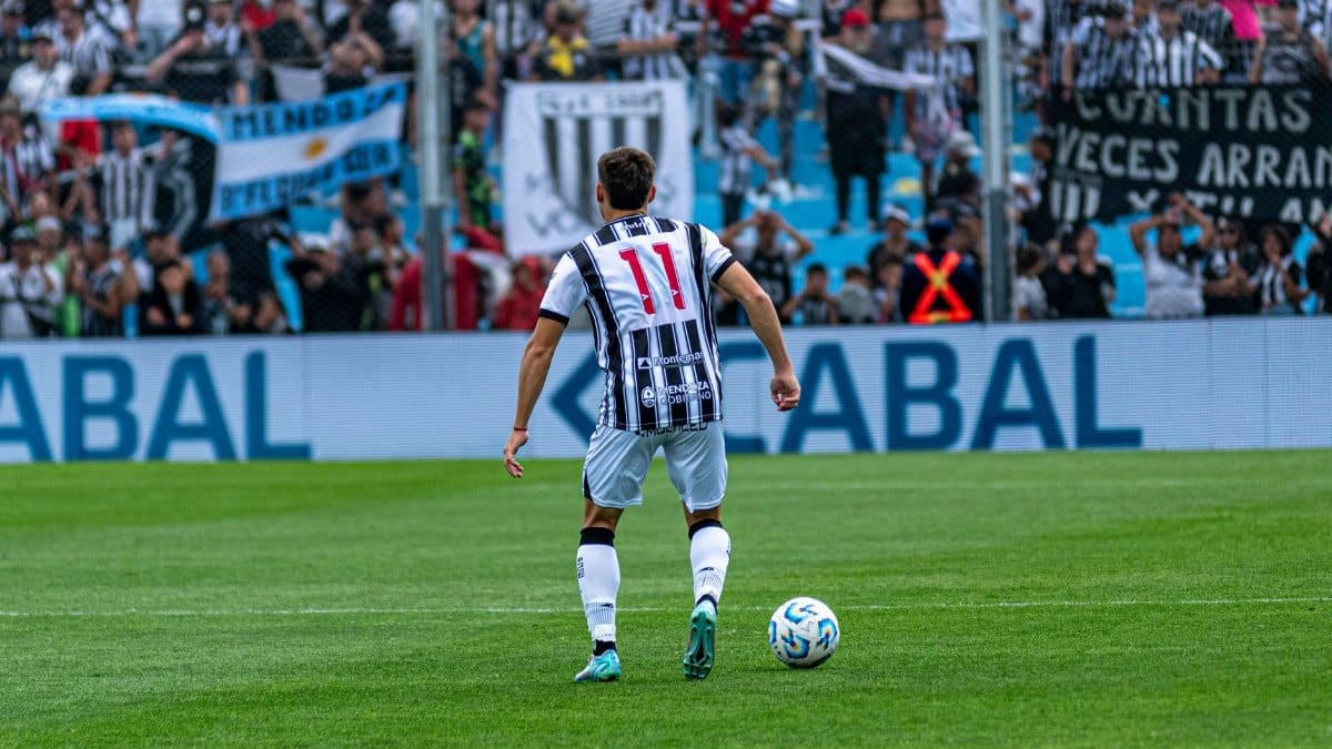 Soccer player number 11 in action on field during a match with cheering fans in the background.