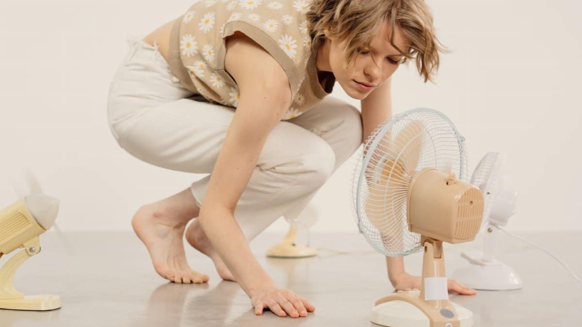 Young woman observing several table fans in minimalist indoor studio setting.