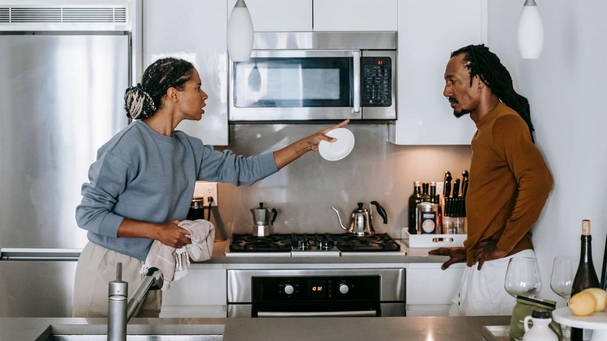 Side view of young displeased ethnic female pointing at serious male partner with hand on hip while looking at each other during conflict