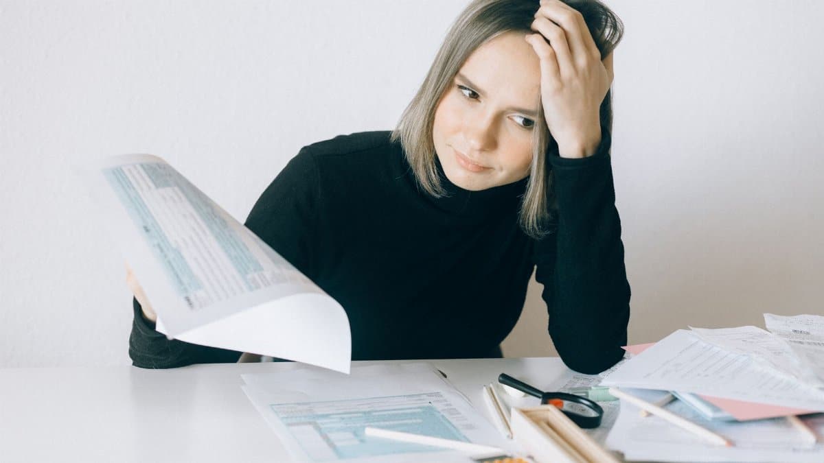 A woman showing stress while reviewing multiple paperwork and financial documents at a desk.