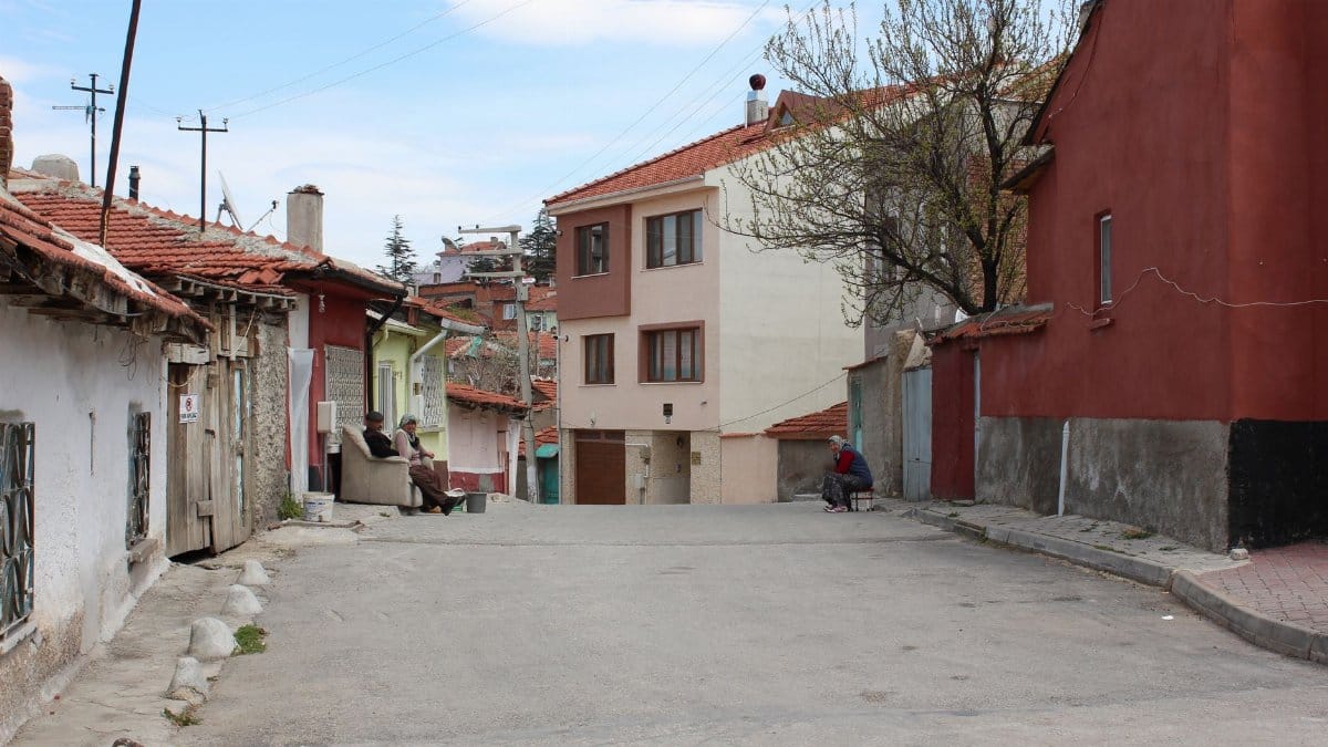 A peaceful street in a rustic neighborhood with people seated and colorful houses.
