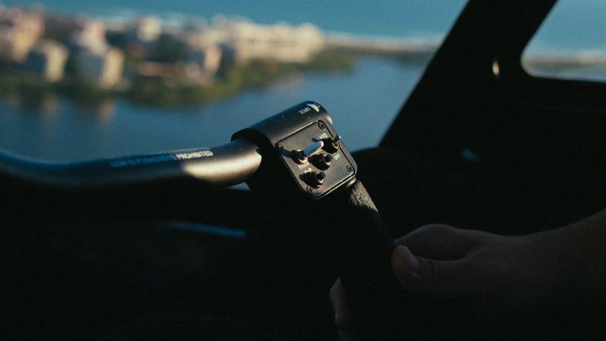 A person's hand gripping an aircraft control inside a cockpit during daytime.
