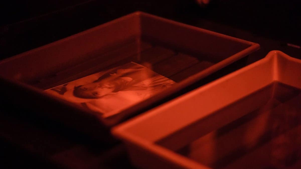 Capturing the classic film development process in a darkroom with trays and red light.