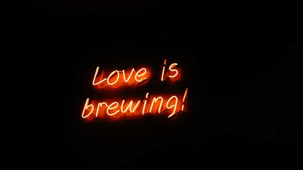 Vibrant neon sign displaying the phrase 'Love is brewing!' captured in a dark setting.