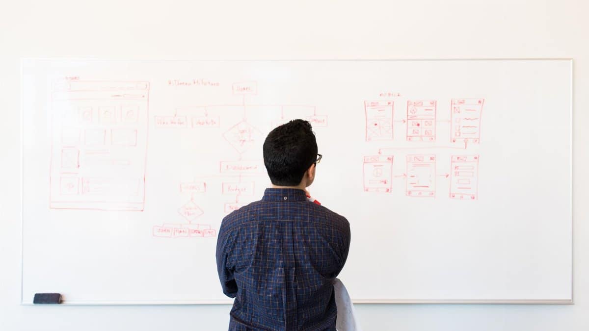 Man standing at a whiteboard planning UX design concepts in a modern office setting.