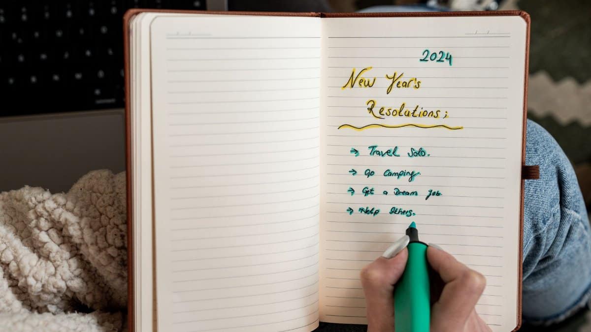 Person making 2024 New Year's resolutions in a notebook with a green marker.