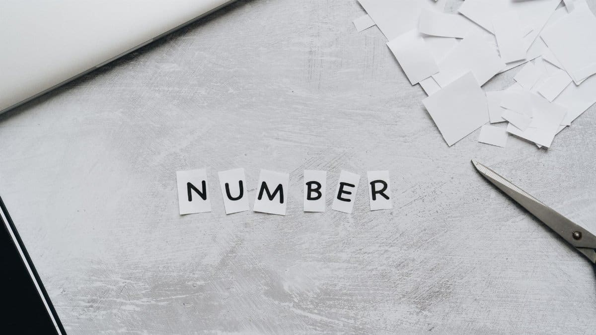 A minimalist desk setup featuring cut-out letters forming the word 'NUMBER' with scissors and paper on a white background.