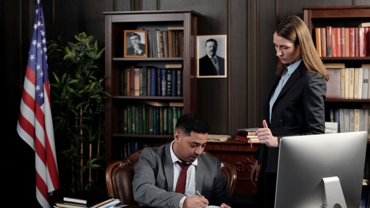 Business professionals discussing documents at a desk in an office with an American flag in the background.