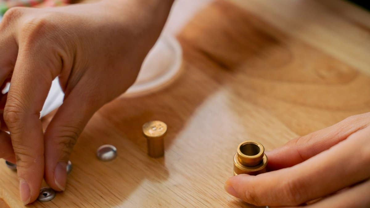 Detailed view of hands working with snap fasteners on a wooden table, showcasing sewing precision.