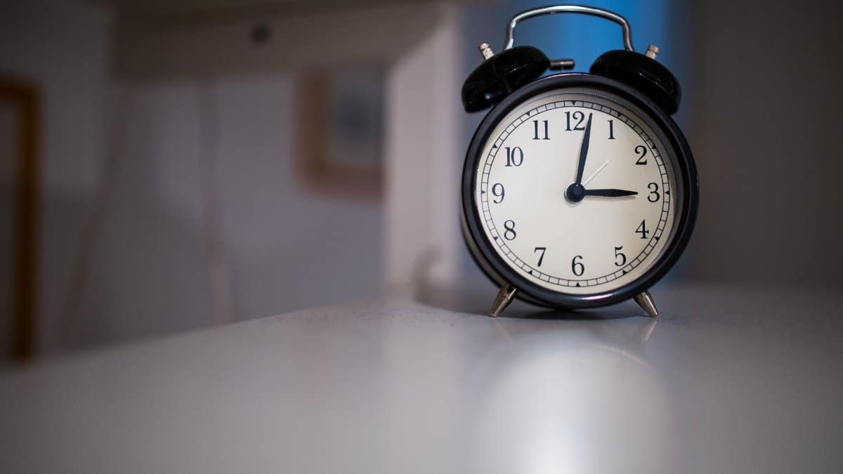 A classic black alarm clock with a white face showing 7:05, placed on a white surface.