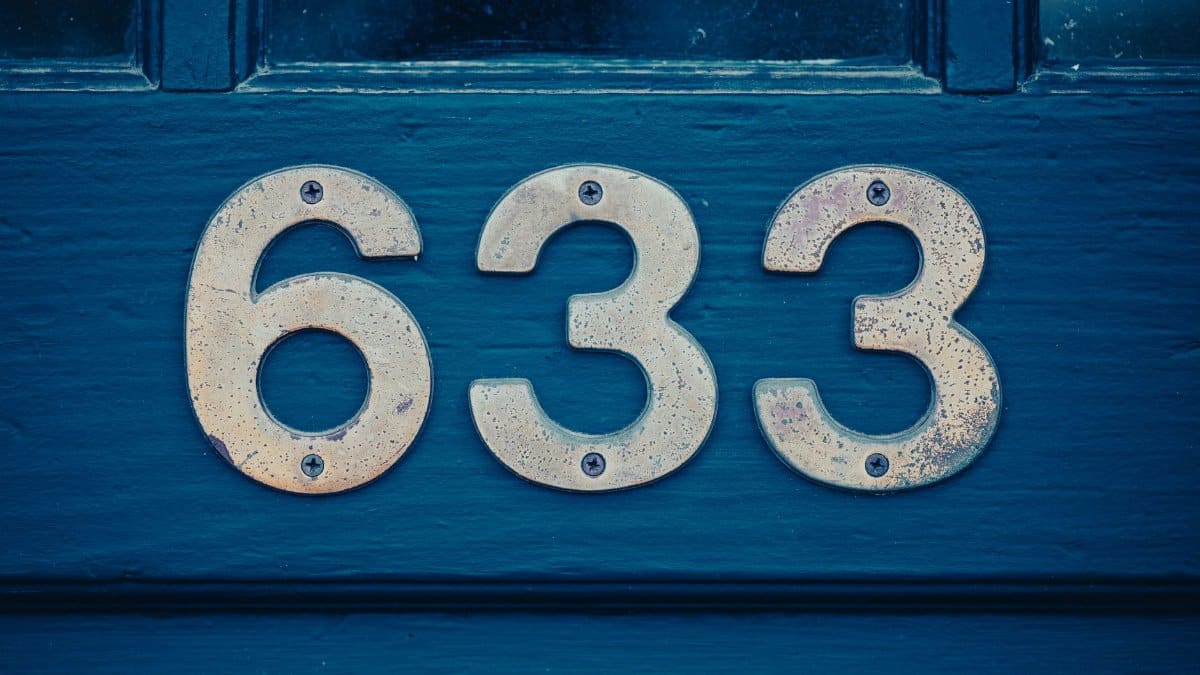 Close-up of rustic metal house number 633 on a weathered blue door.