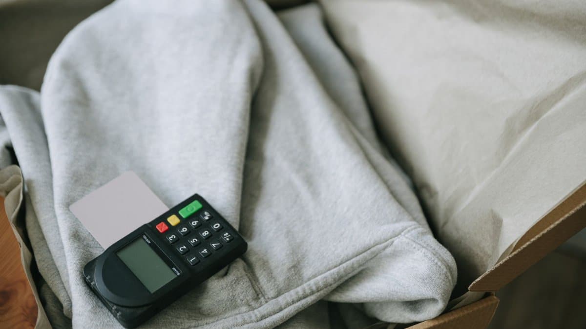 A payment terminal and card placed on folded clothing inside a shipping box, indicating e-commerce packaging.