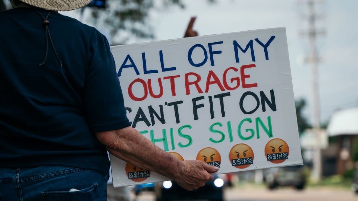 Person at a protest holding a sign expressing their outrage. Outdoors setting.