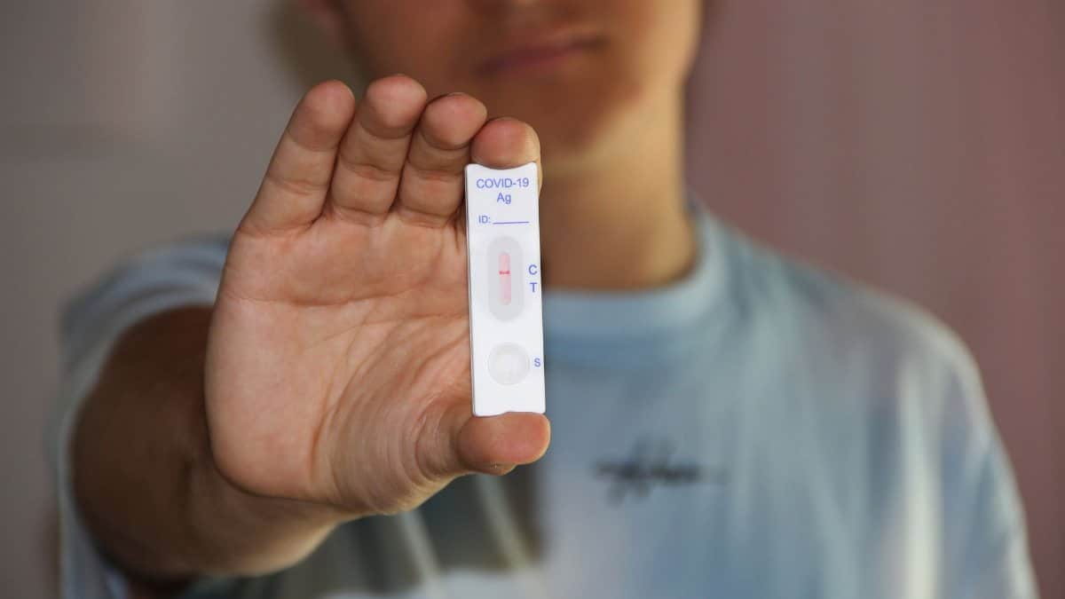 Close-up of a man holding a COVID-19 antigen test kit indoors.