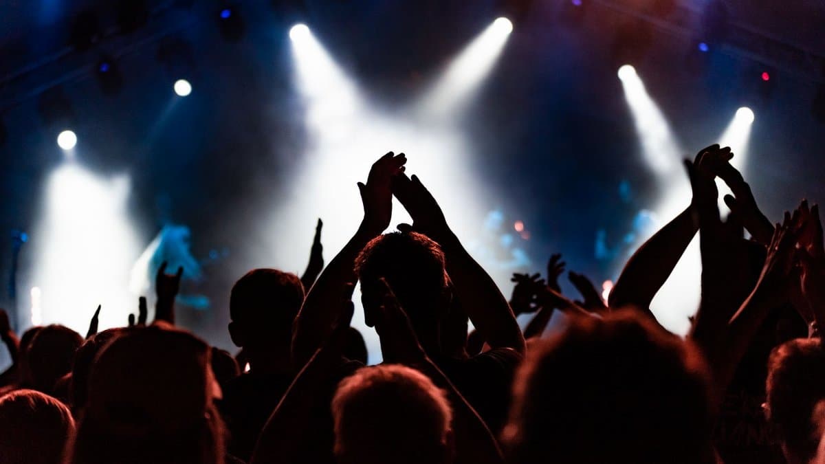 Silhouetted concert crowd clapping and cheering under bright stage lights during a dynamic music performance.