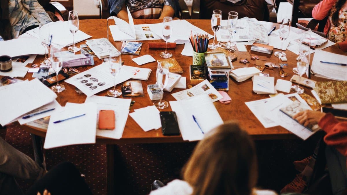 Group collaborating at a cluttered conference table filled with documents and drinks.