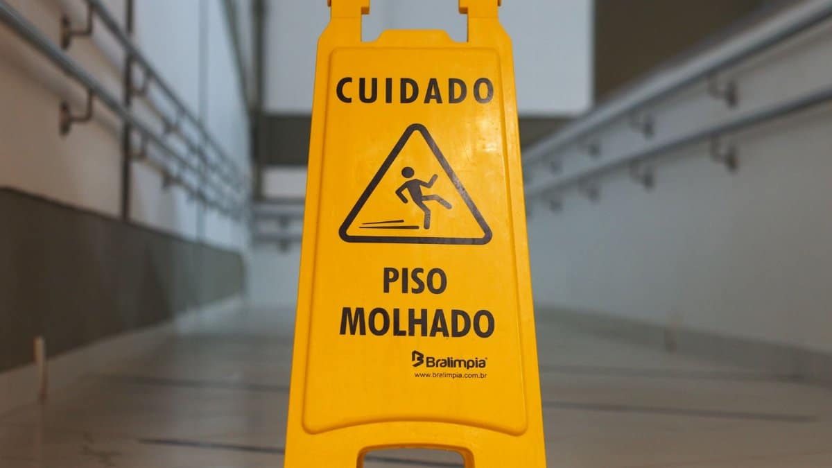 Bright yellow caution sign signals wet floor in a corridor with tiled flooring.