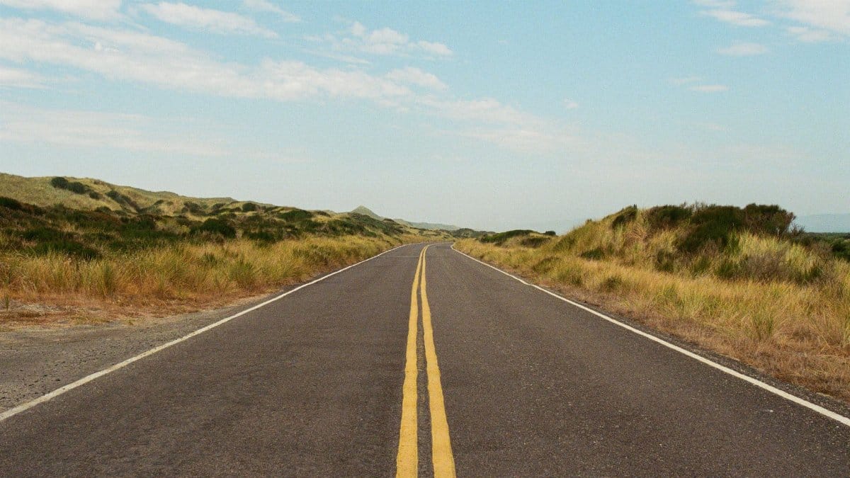 Long open road stretching through the scenic countryside beneath a clear sky.