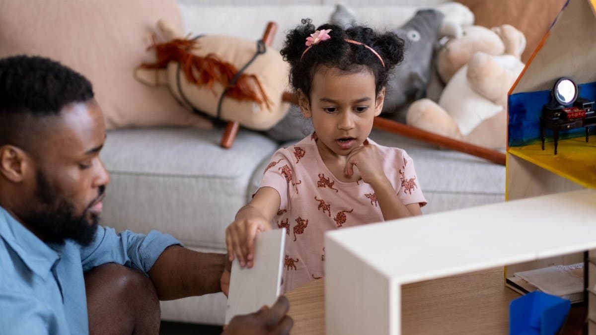 A father and daughter enjoy family time playing with a dollhouse indoors, fostering creativity and togetherness.