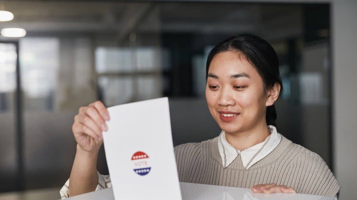 Asian woman placing a ballot paper into a box during an indoor voting session.